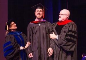大研究生在毕业典礼上站在两位教授之间微笑.